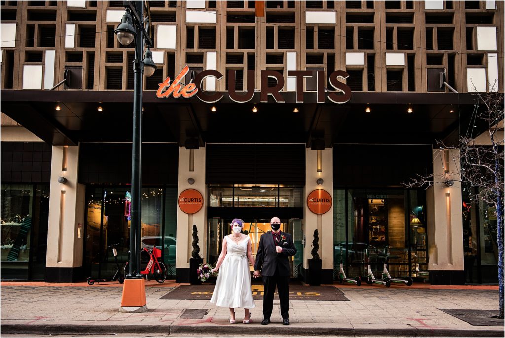 Bride and groom stand in front of the Curtis Hotel at their wedding during COVID-19