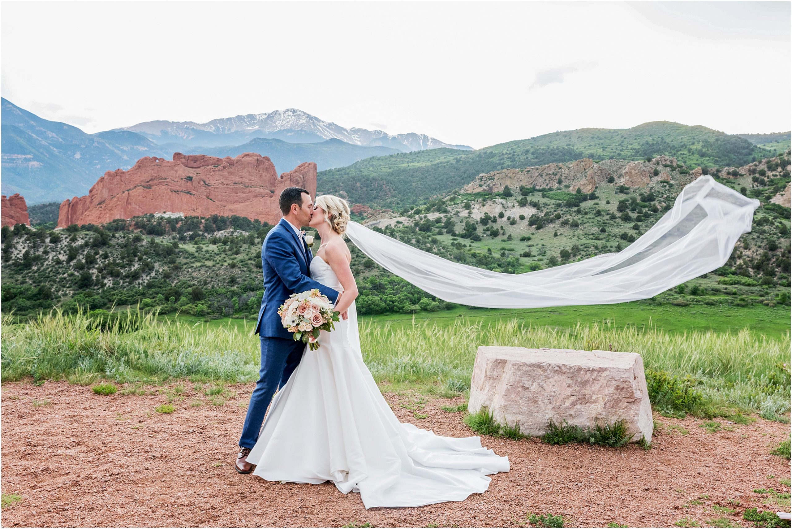 Bride and groom kiss and embrace while brides vail flies in the air with stunning mountain views