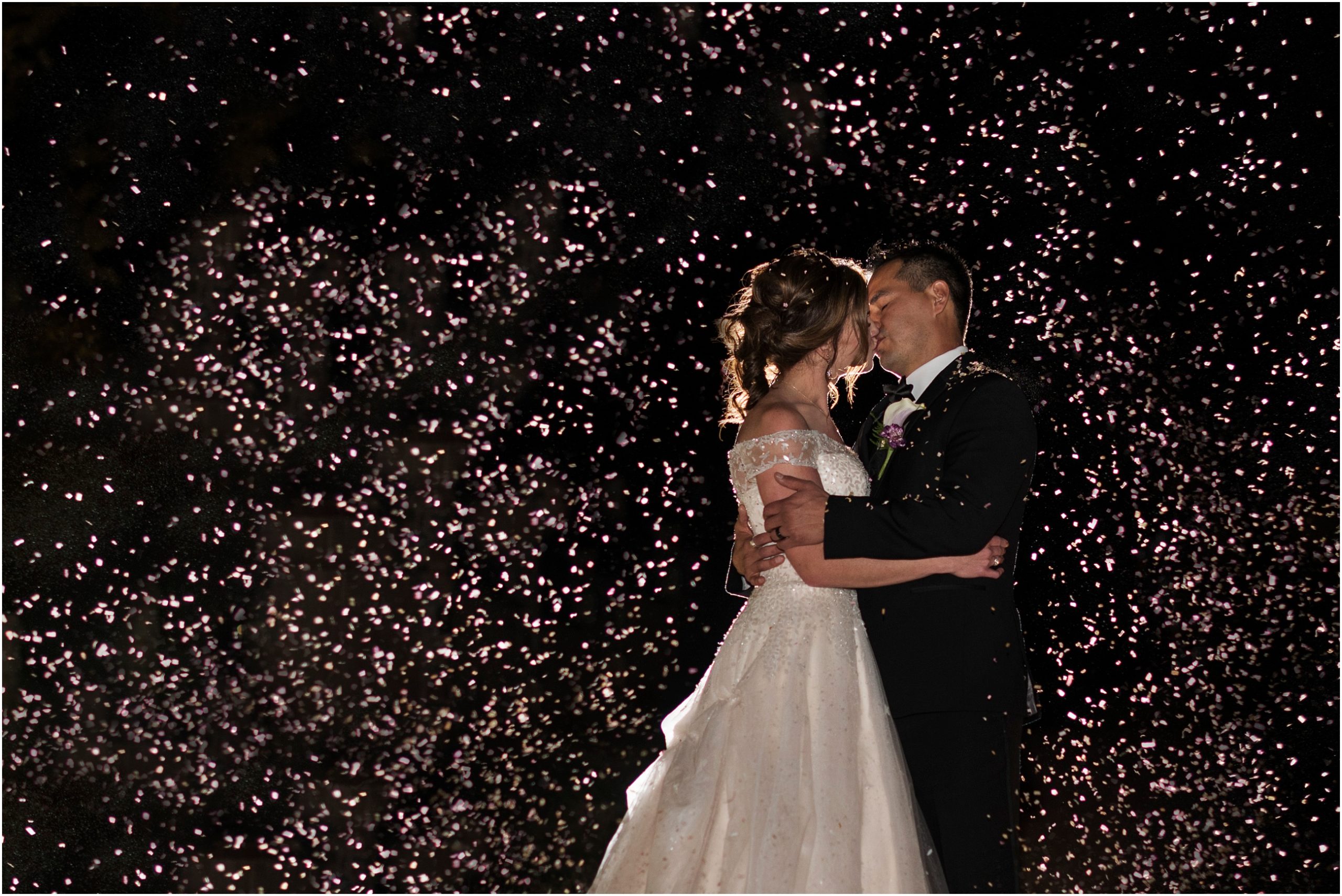 A wedding couple kisses passionately in front of purple confetti behind them on their wedding night
