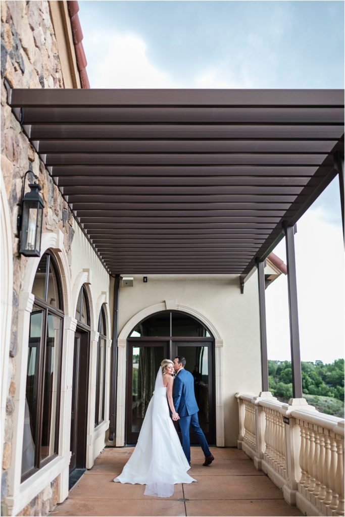 Groom kisses brides cheek while they hold hands on the balcony at The Pinery in Colorado