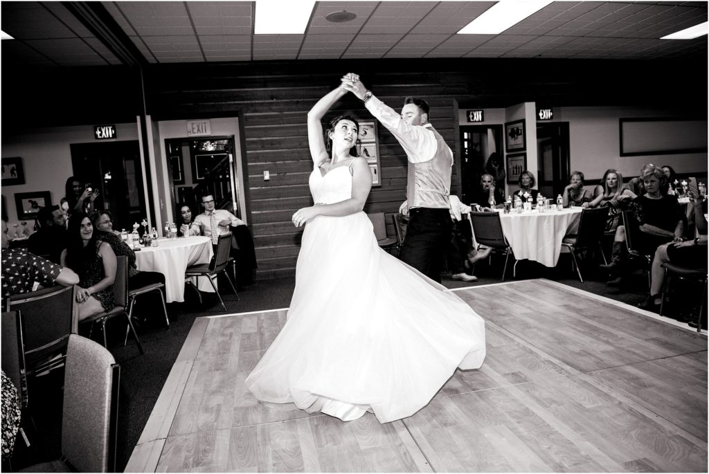 First wedding dance photo of groom twirling his bride on indoor wooden dance floor