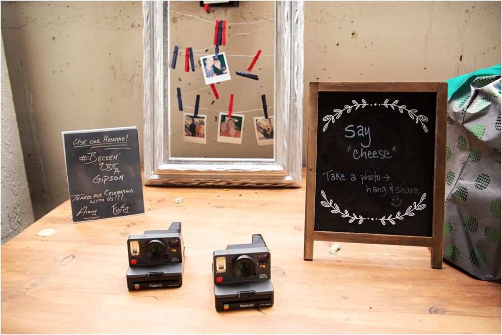Chalkboard sign and polaroid cameras serve as a guest book bride and groom hashtag is provided for guests to send pictures
