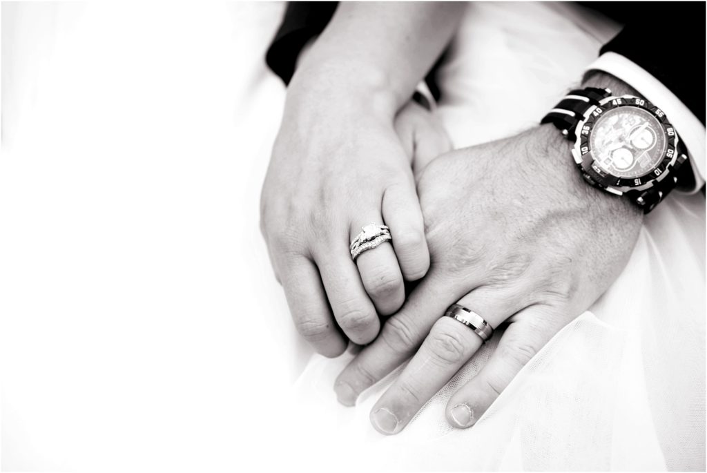 Black and white photo of the bride and groom holding hands showcasing wedding rings