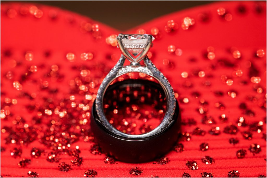 Bride and groom wedding rings displayed together in front of stunning red tea ceremony dress captures all the sparkle