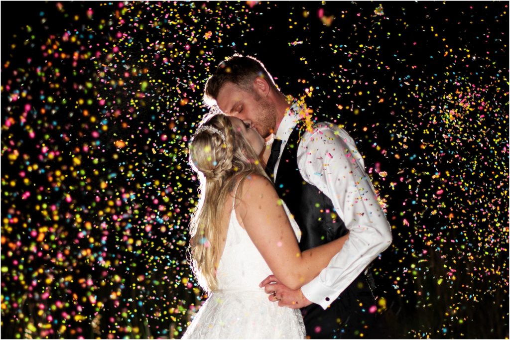 Magical nighttime wedding photo of the bride and groom kissing with confetti all around them creates a playful look