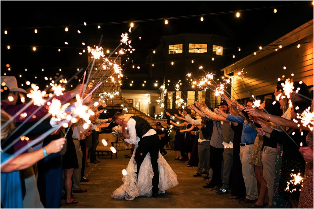 Bride and groom exit through a sparkler tunnel created by wedding guests for their send-off