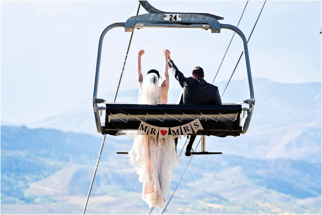 Wedding photographer, Tina Joiner captures the couple celebrating on a ski lift with bride and groom printed on an attached banner in Granby, Colorado wedding