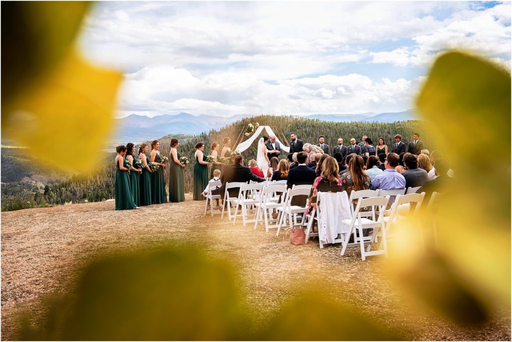 Unique wedding ceremony photo captures golden Aspen leaves, mountain peaks and wedding ceremony at mountain top outdoor wedding