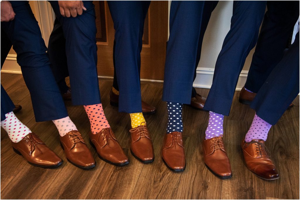 Groom's gift of multi-colored polka dot socks pop beneath navy blue suit pants and make for a fun wedding photo