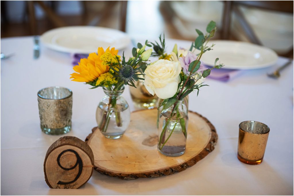Rustic natural wedding reception centerpieces are made up of live edge wood splices, wooden table number and simple low-profile floral arrangements