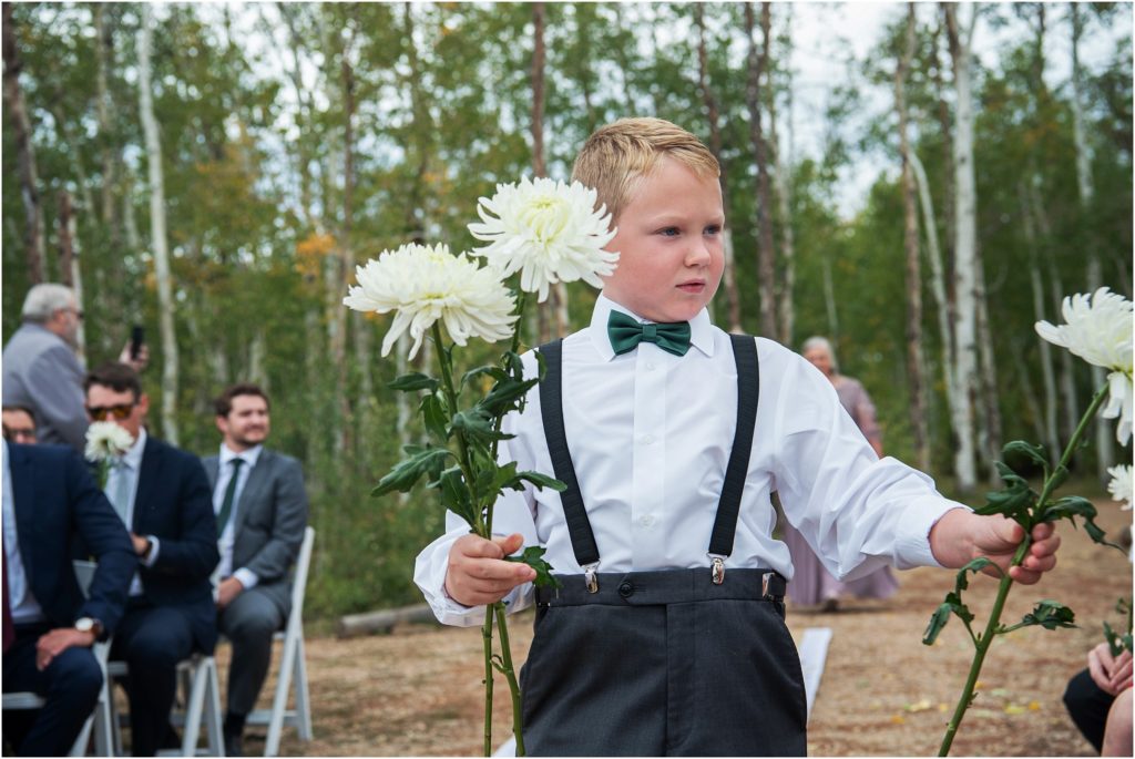 As an alternative to carrying a pillow down the aisle, this ring bearer hands out flowers to guests as he makes his way down the aisle in his green bow tie and black suspenders.