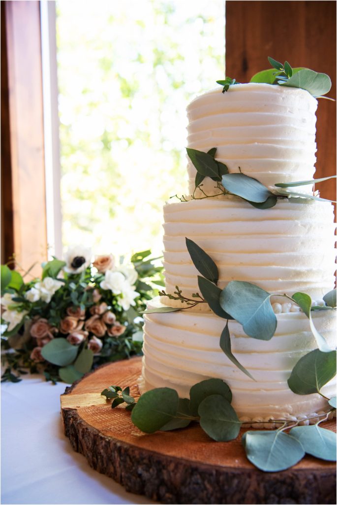 White wedding cake with eucalyptus leaves sits atop a natural wood cake stand