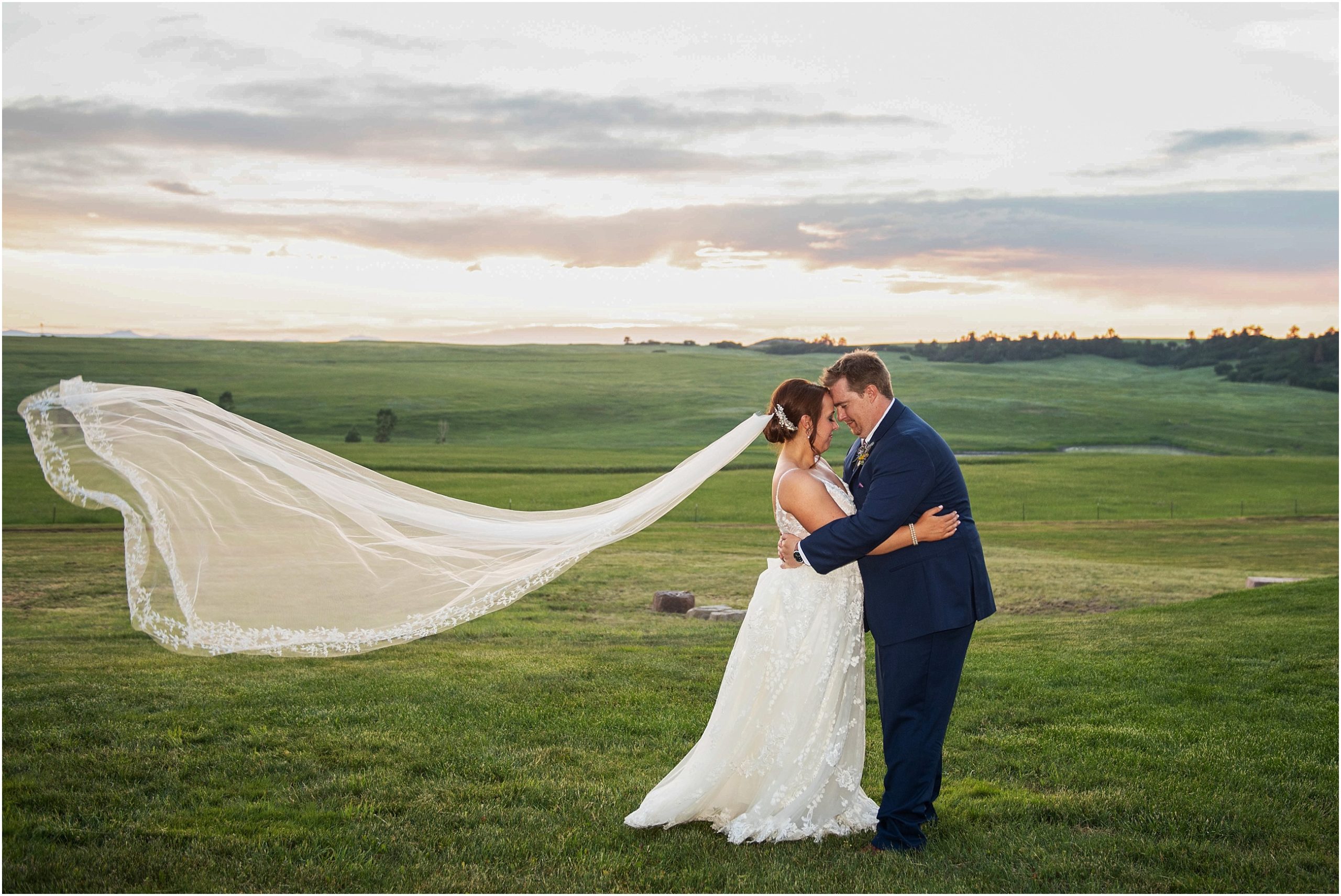 Bride and groom pose for a stunning photo with the bride's veil swooping behind her on this Colorado summer evening