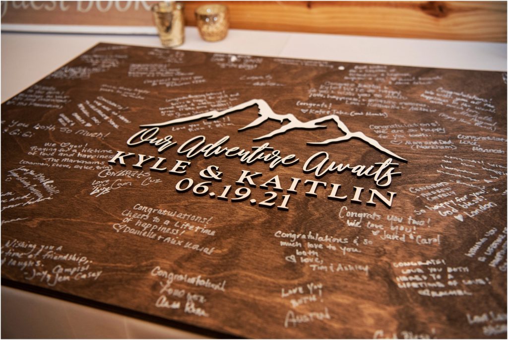 Nontraditional wedding guest book where guests signed a stained wooden sign with the couple's names, the wedding date and the quote our adventure awaits