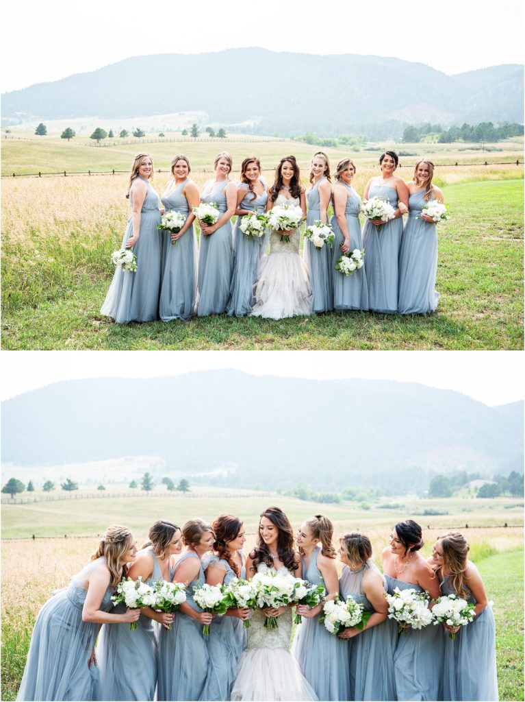 Bridesmaids wear a variety of styles in a dusty blue color holding all white bouquets standing in a field with mountains behind them
