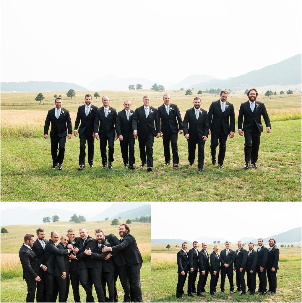 Groom with eight groomsmen walk and hug in a field wearing black suits with light blue ties in this wedding at Spruce Mountain Ranch with a large wedding party