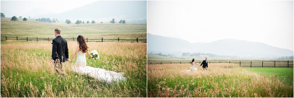 Bride and groom walk holding hands in tall grass on their wedding day with mountains and haze in the distance