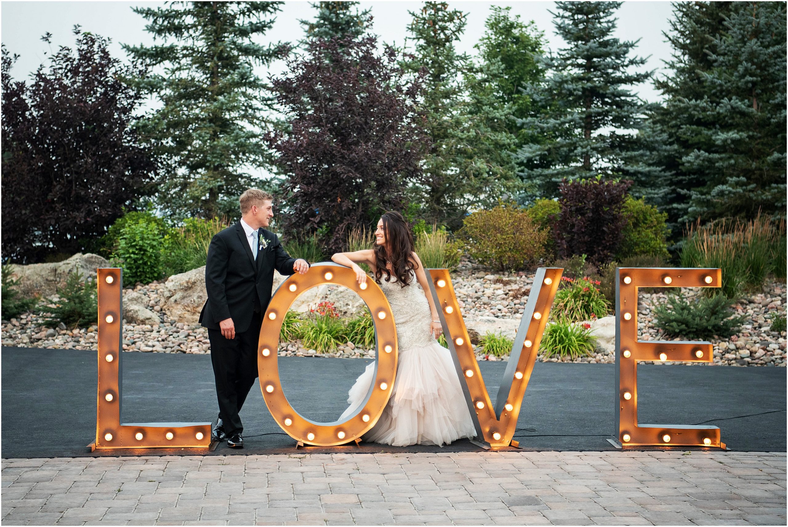 Bride and groom stand by their huge lit up LOVE letters looking at each other