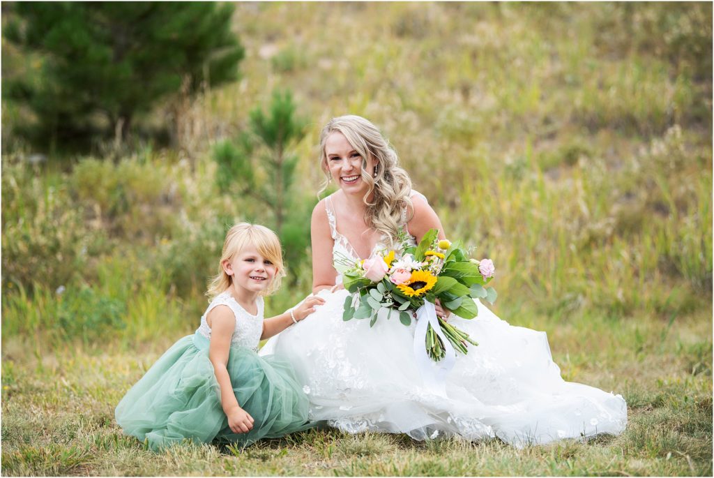 Bride and flower girl sit together in the grass at a wedding