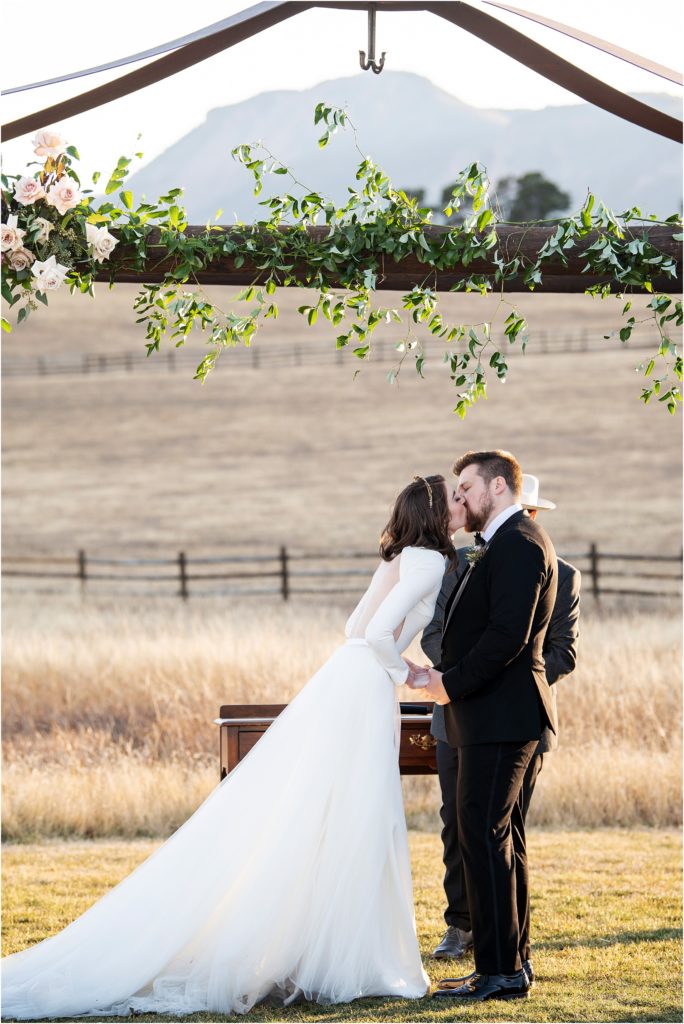 Bride and groom kiss during their outdoor wedding ceremony at a ranch in colorado