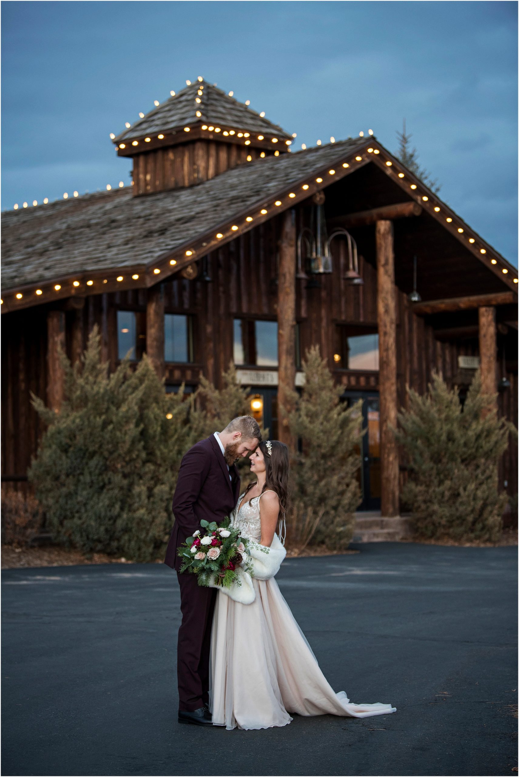 Bride and groom embrace in front of Alberts lodge at dusk at their December wedding.