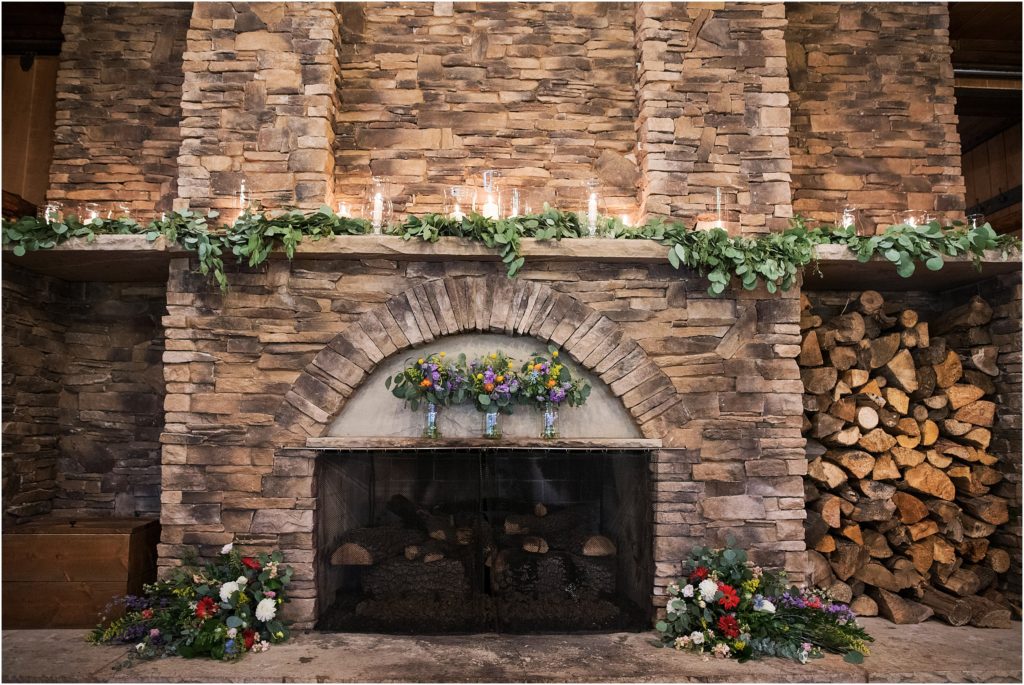 Beautiful florals and greenery and candles are used to decorate a huge fireplace in a lodge in Colorado at a wedding