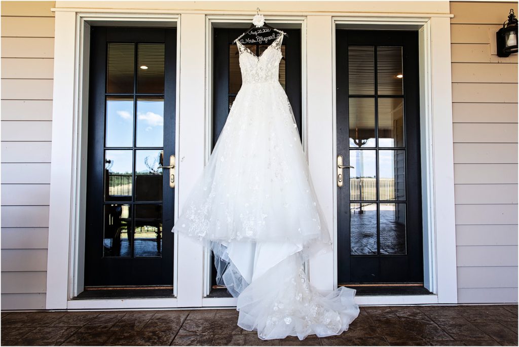 Wedding dress hangs on door frame with custom made hanger moments before her wedding