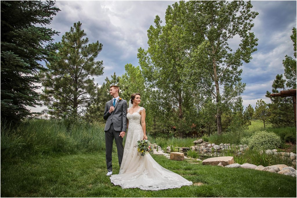 Bride and groom stand in green grass surrounded by trees on their summer wedding day at Spruce Mountain Ranch in Colorado