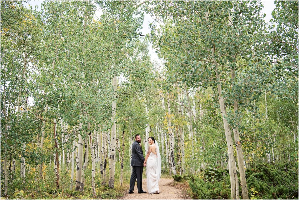 Bride and groom walk holding hands through the Aspen trees in the fall in Granby, Colorado, on their wedding day.