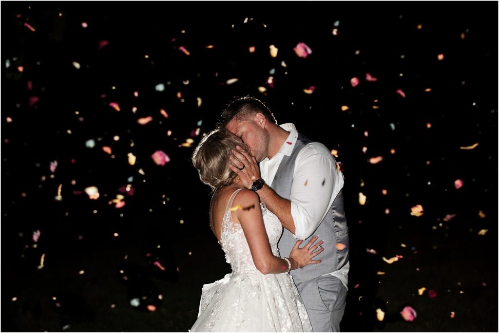 Bride and groom kiss at night while confetti is thrown around them