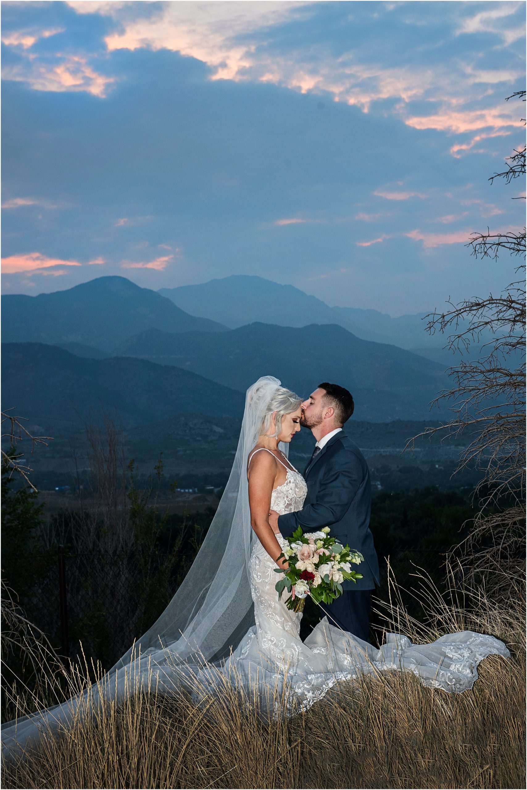 Bride and groom stand with mountains behind them after sunset as the sky shows off in colors of blue and pink with hints of purple